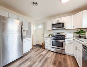 A modern kitchen with stainless steel appliances, white cabinetry, and a herringbone wood floor.