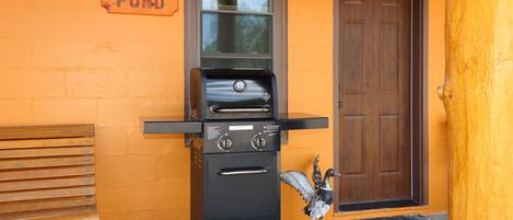 Una parrilla exterior negra, un banco de madera, una puerta y un cartel que dice 'DUCK POND'.