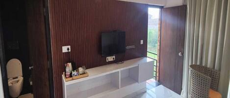 A hotel room with a bed, a television mounted on the wall, a small seating area, and a balcony with curtains.