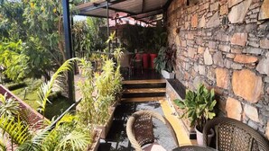 Un espacio al aire libre techado, con paredes de piedra, plantas en macetas y mobiliario de mimbre.