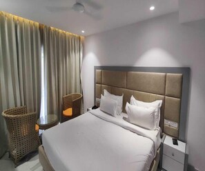 A hotel room with a large bed, a headboard, a nightstand, a wicker chair, and a window with curtains.