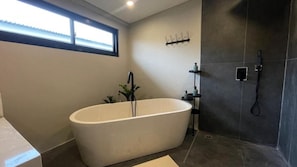Een moderne badkamer met een vrijstaand bad, een douchegedeelte en een raam voor natuurlijk licht.