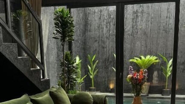 Ein modernes Wohnzimmer mit einem grünen Sofa, einem runden Couchtisch und Blick auf einen Pool durch große Fenster.