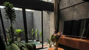 Ein modernes Wohnzimmer mit einem grünen Sofa, einem Flachbildfernseher und Topfpflanzen.