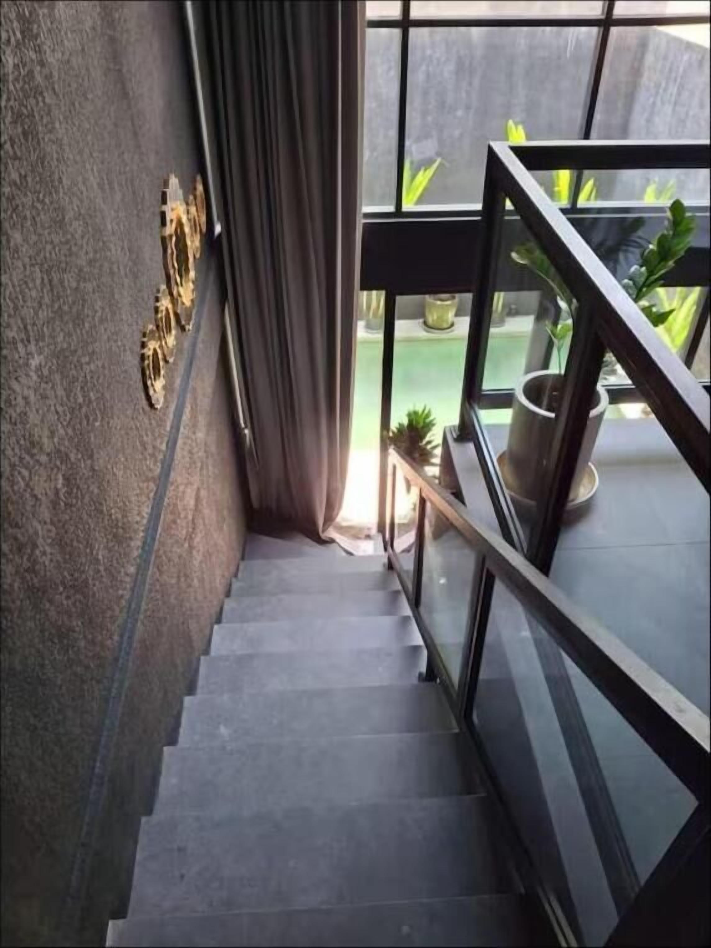 A staircase leading to a balcony with potted plants, a glass railing, and a view of the outside.