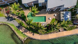 Vista aérea de un resort con piscina, palmeras y un edificio moderno con techo inclinado.