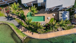Ein Luftbild eines Resorts mit Swimmingpool, Palmen und einem modernen Gebäude mit geneigtem Dach.