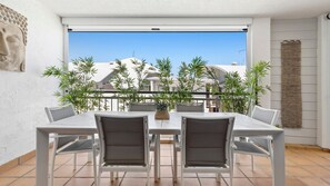 Eine Terrasse mit Tisch und Stühlen, umgeben von Pflanzen, mit Blick auf Gebäude im Hintergrund.