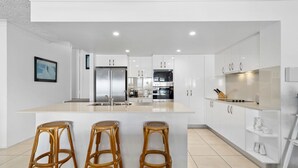 Una cocina moderna con armarios blancos, una isla central con taburetes, electrodomésticos de acero inoxidable y un cuadro en la pared.