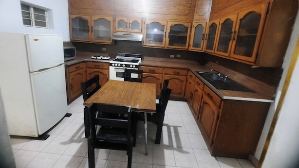 Una cocina compacta con armarios de madera, una estufa, un refrigerador y una mesa de comedor con sillas.