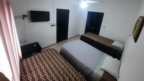 Una habitación con dos camas, ventilador de techo, televisor montado en la pared y una mesita.