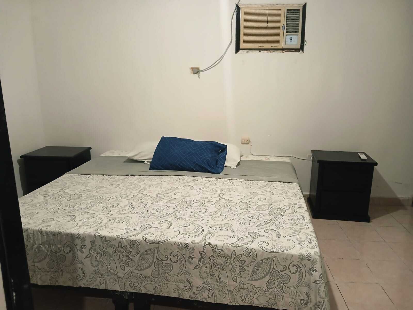 Ein Schlafzimmer mit Bett, Nachttisch, Wandairconditioner und Steckdose.
