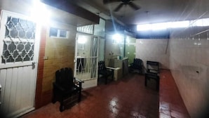 Una habitación con ventilador de techo, una puerta con panel de vidrio, un banco y una pequeña mesa.
