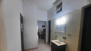 Un pasillo estrecho con un lavabo y un espejo a la derecha, que conduce a una habitación con una puerta al final.