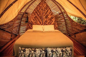 Ein Bett in einer zeltähnlichen Struktur mit einem Kissen mit Blattmuster und einem schlichten Kissen.