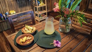 A wooden table with a pitcher of yellow drink, a bowl of fruit, and a vase with flowers. - Qasa Boutique Hotel and Retreats - LGBTQ (Barú)