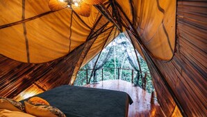 A tent with a bed, a hanging light fixture, and a view of trees through the entrance. - Qasa Boutique Hotel and Retreats - LGBTQ (Barú)