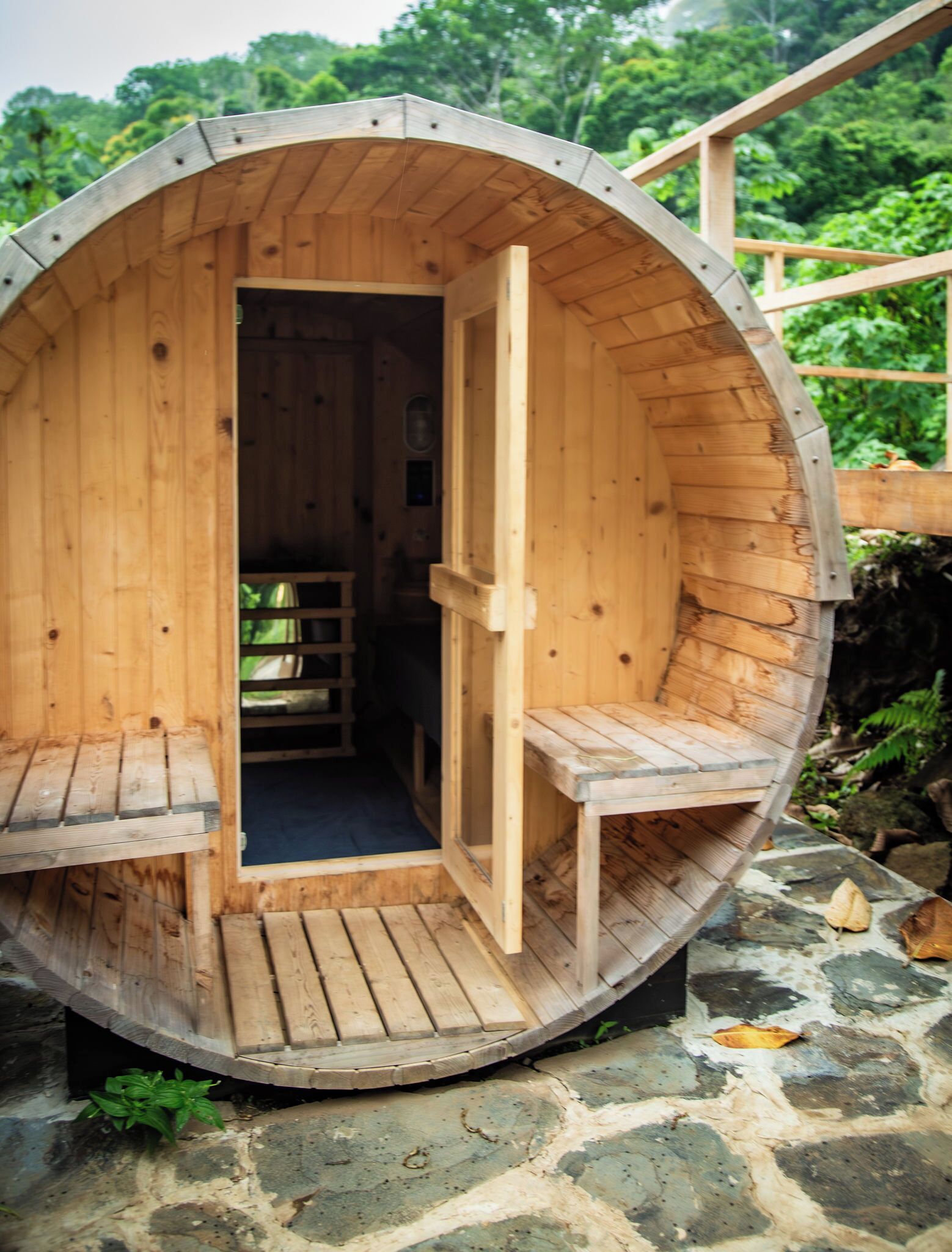 Una sauna de madera con un banco y una puerta, ubicada sobre una base de piedra.