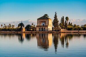 A building with a central archway, surrounded by palm trees and a calm body of water reflecting the structure. - Palais Talilit (Marrakech)