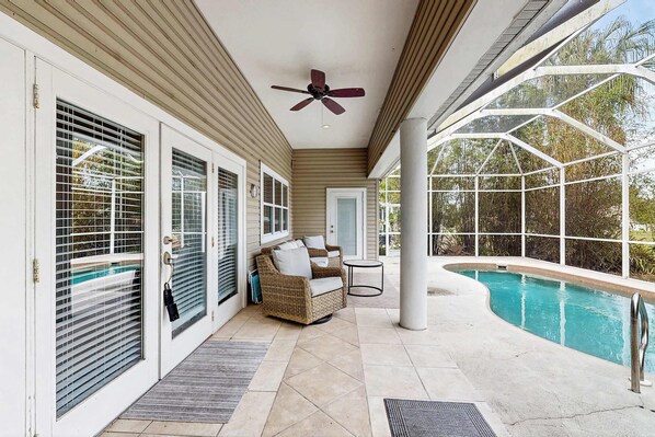 Eine überdachte Terrasse mit Pool, Deckenventilator und Rattan-Sofa.