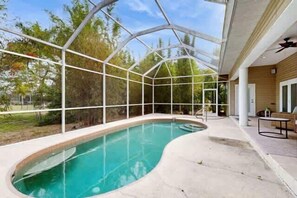 Ein Schwimmbad mit Glasüberdachung, umgeben von einer Holzterrasse und einer überdachten Terrasse.