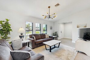 A modern living room with a sofa, coffee table, and a TV. There are windows, a plant, and a lamp. - Port Charlotte Oasis Private Pool Home with Spacious Kitchen (Port Charlotte)