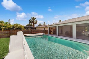 A backyard with a swimming pool, a wooden fence, and a house with large windows. - Port Charlotte Oasis Private Pool Home with Spacious Kitchen (Port Charlotte)