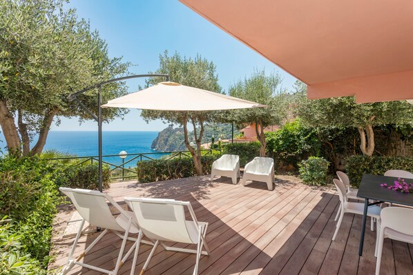A wooden deck with outdoor furniture, a table, and a view of the sea.