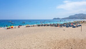 A beach with rows of sun loungers and umbrellas, boats on the water, and a hilly landscape in the background. - Apartment 'Paradise Residence 1' with Sea View, Wi-Fi and Air Conditioning (Sant'Alessio Village)