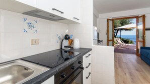 A modern kitchen with a black countertop, white cabinets, and a view to a balcony with outdoor furniture. - Apartment 'Paradise Residence 1' with Sea View, Wi-Fi and Air Conditioning (Sant'Alessio Village)