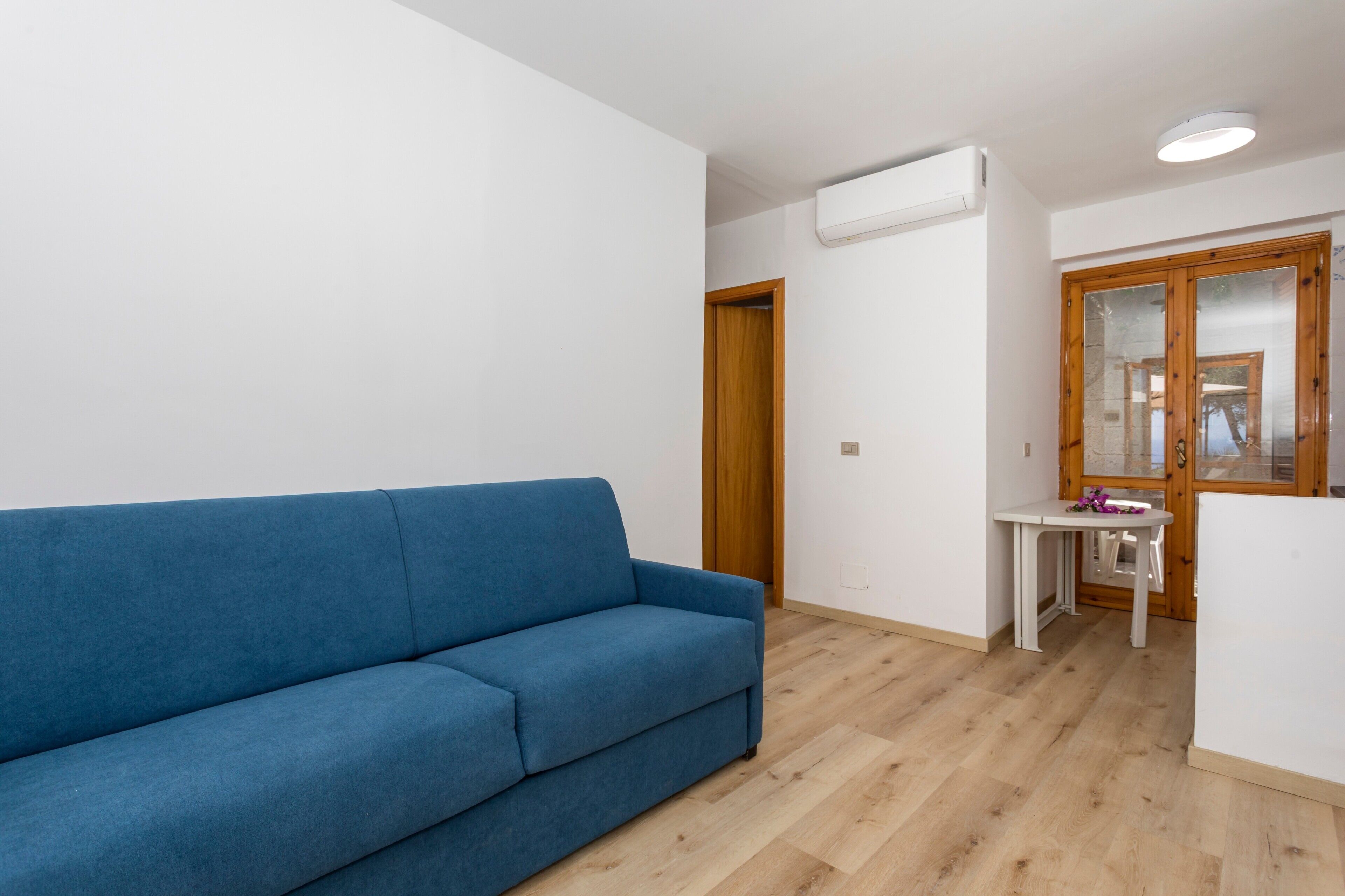 Une pièce avec un canapé bleu, une petite table blanche et une porte en bois.