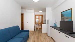 A compact living space with a sofa, kitchenette, and a painting on the wall. - Apartment 'Paradise Residence 1' with Sea View, Wi-Fi and Air Conditioning (Sant'Alessio Village)