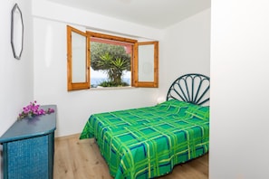 A bedroom with a bed, a window with a view, a dresser, and a chair.