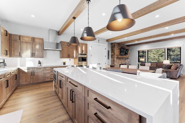 A modern kitchen with wooden cabinets, a large island, pendant lighting, and a stone fireplace.