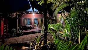 A well-lit building with a wooden deck, surrounded by lush greenery. - Cabañas Kai  (Iztapa)
