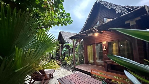 A wooden building with a thatched roof, surrounded by greenery and outdoor seating. - Cabañas Kai  (Iztapa)