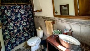 A bathroom with a toilet, a sink, a mirror, and a shower curtain. - Cabañas Kai  (Iztapa)