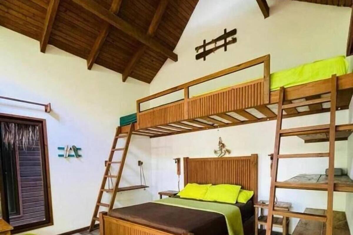 Una habitación con literas, una escalera, una mesita y una ventana con persianas.
