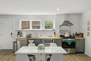 A modern kitchen with a white table, stainless steel appliances, and a window with wooden blinds. - Urban oasis, Central District - Studio (Seattle)