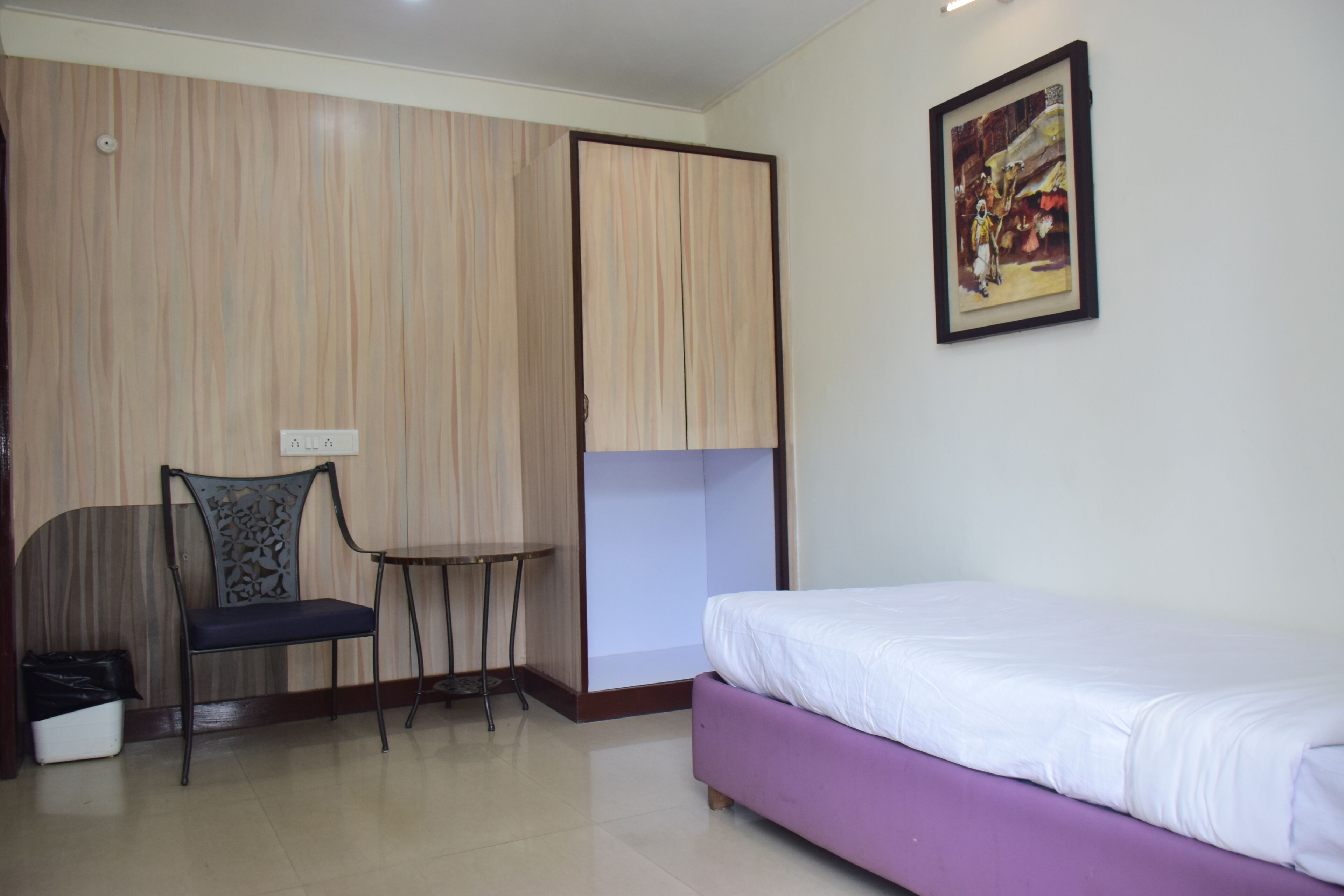 A room with a bed, a chair, a small table, and a wardrobe.