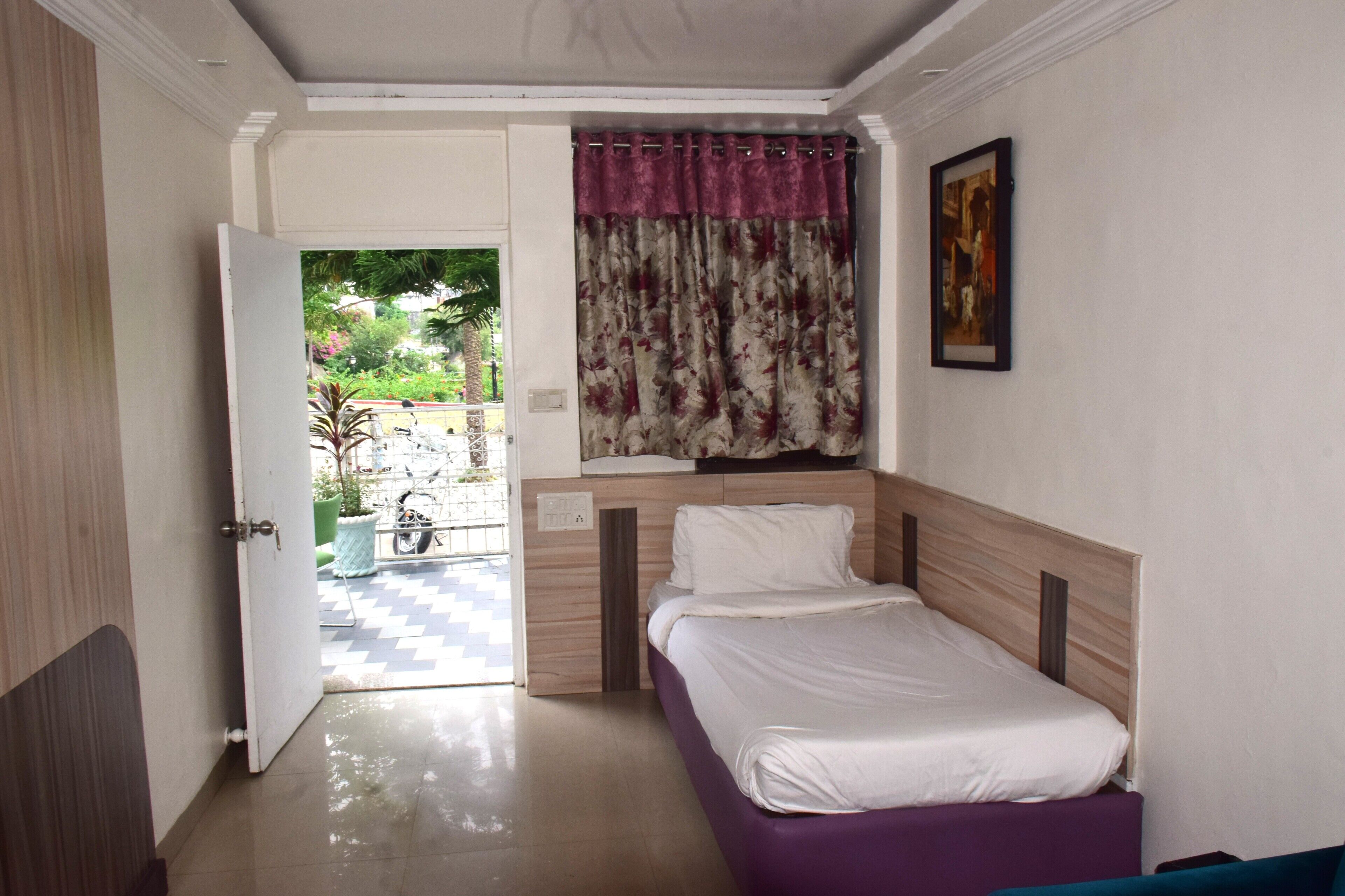 A room with a bed, a door leading outside, a window with curtains, and a wall-mounted picture.