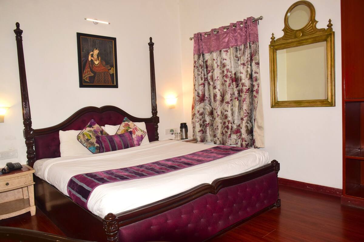 A bedroom with a four-poster bed, a large mirror, and a painting on the wall.