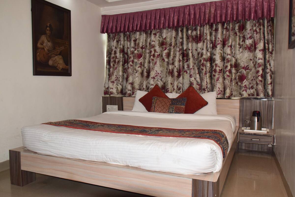 A neatly made bed with a patterned bedspread, a nightstand with a lamp, and a painting on the wall.