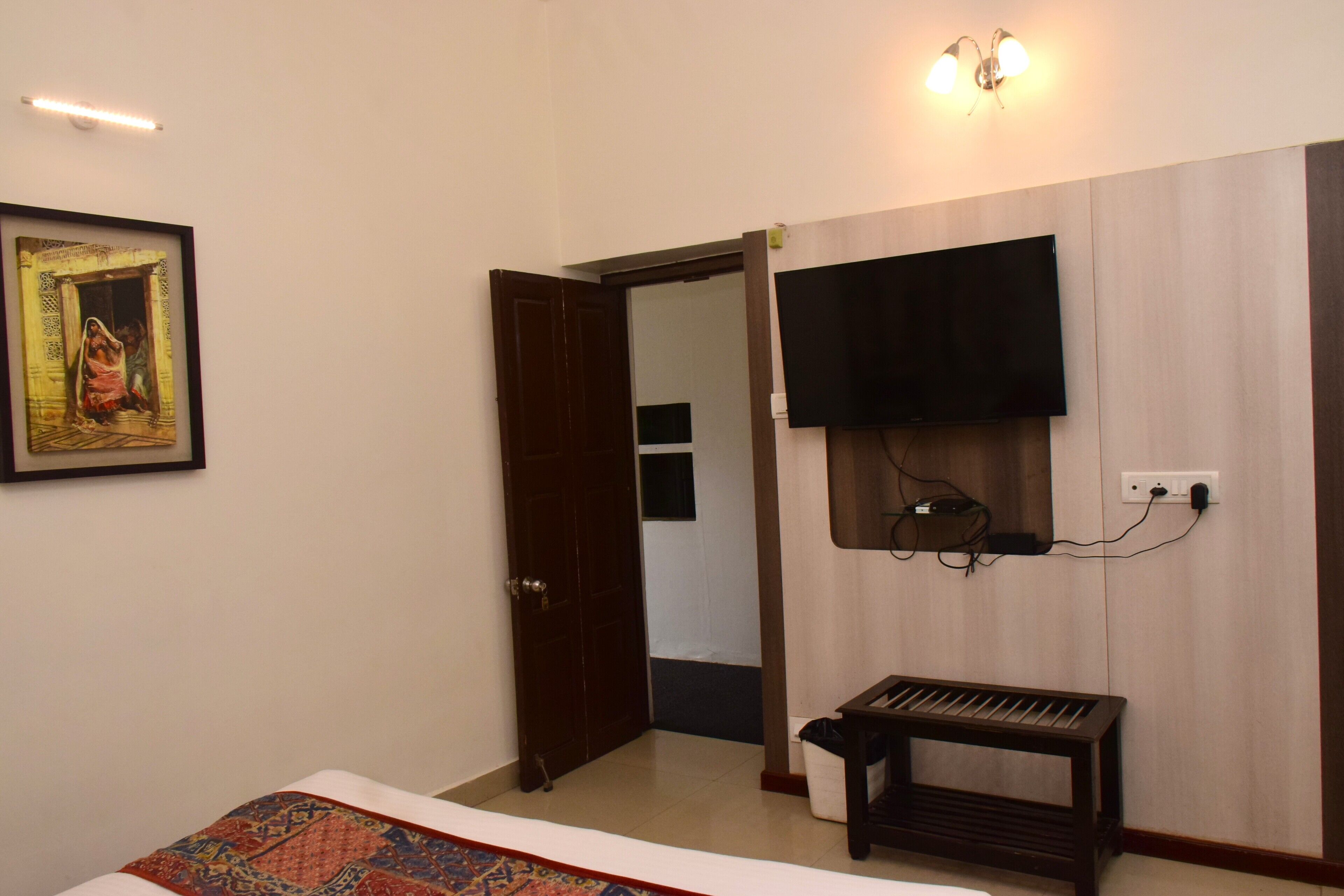 Habitación de hotel con cama, televisión montada en la pared, una puerta y una mesita.