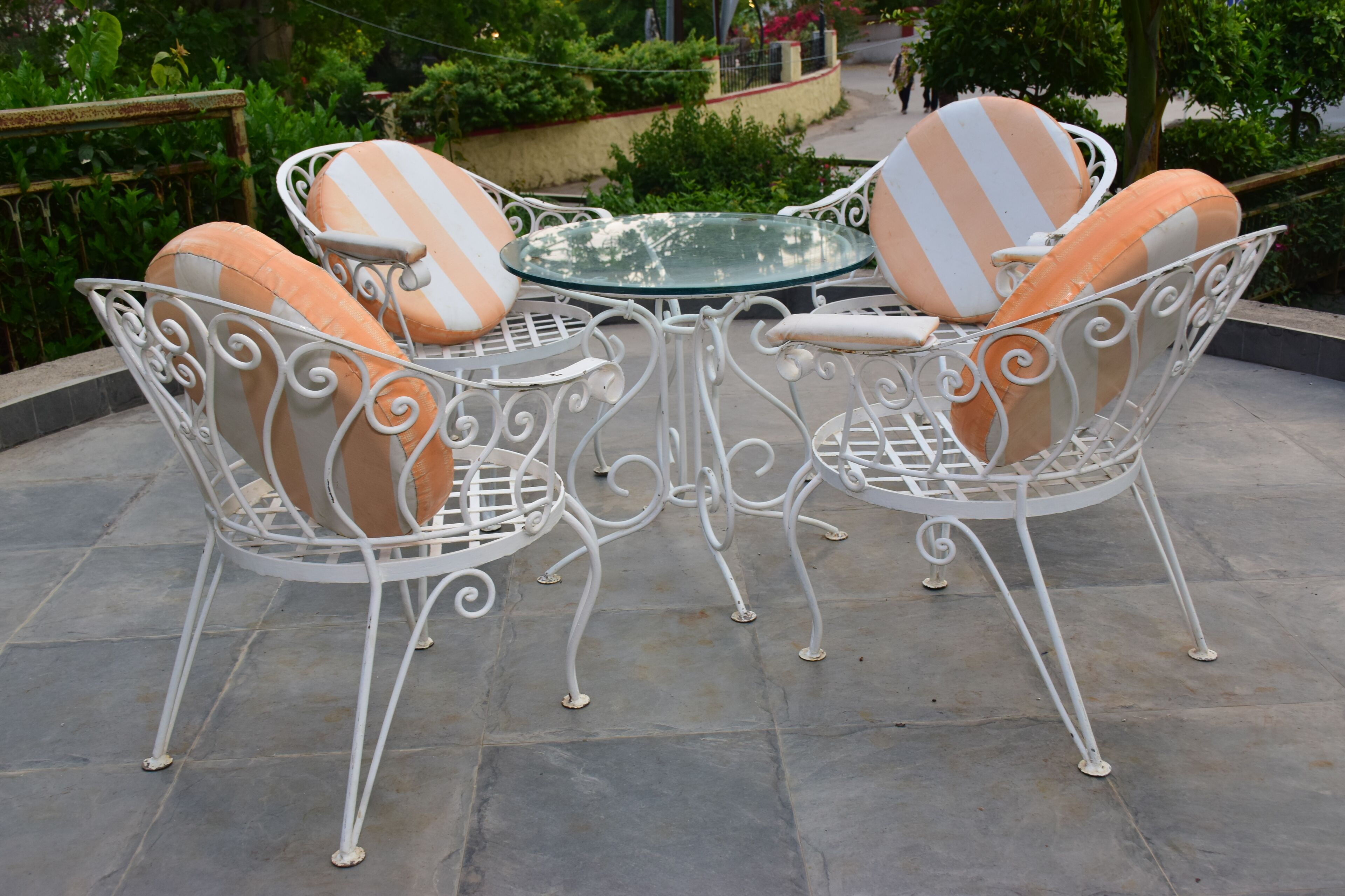 A metal outdoor table with chairs, surrounded by greenery.