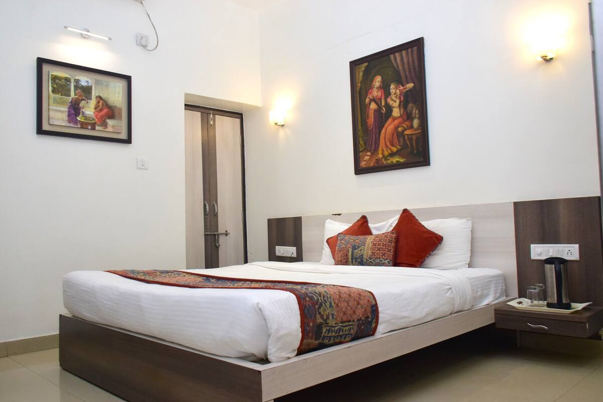 A hotel room with a bed, nightstand, wall-mounted artwork, and a door.