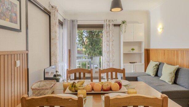 A dining area with a table set for breakfast, a sofa, and a view of the outdoors. - #367 Cozy Orion Apartment | Pool & Balcony (Albufeira)