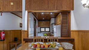 A dining area with wooden paneling, a kitchen in the background, and breakfast items on the table. - #367 Cozy Orion Apartment | Pool & Balcony (Albufeira)
