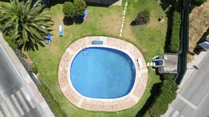 An aerial view of a circular swimming pool surrounded by a brick deck, with a palm tree and a few chairs visible. - #367 Cozy Orion Apartment | Pool & Balcony (Albufeira)
