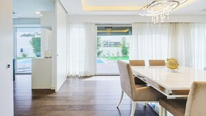 A modern dining room with a white table, beige chairs, and a chandelier.